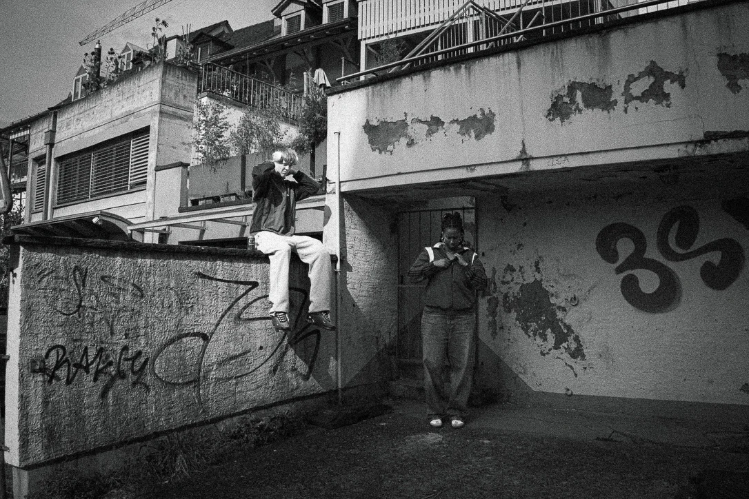 Black-and-white street photograph of two people beside a weathered building